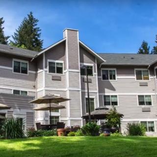 A multi-story residential building surrounded by trees and a grassy area under a clear blue sky.
