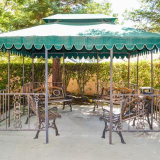 A green-canopied gazebo with outdoor seating in a garden setting.