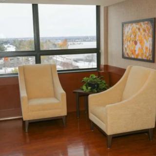 A cozy waiting area with two beige chairs, a small table with a plant, and a large window.