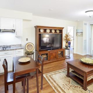 A cozy open-concept living area featuring a dining table, large TV on a wooden stand, and kitchen space.