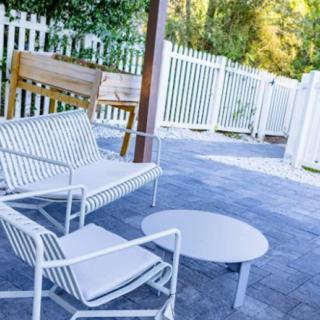 A cozy outdoor patio setup with white furniture and a wooden bench against a fenced backdrop.