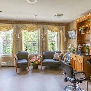 A cozy waiting room with comfortable chairs and large windows adorned with curtains, featuring wooden bookshelves and a television.