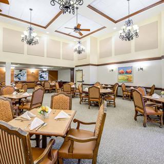A spacious dining room with elegant wooden furniture, chandeliers, and ceiling fans.