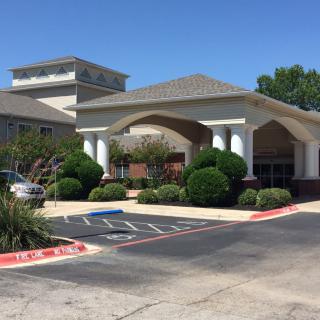 A building entrance with a landscaped area and parking lot during daytime.