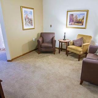 A cozy living room with comfortable armchairs, a sofa, a lamp, and framed artwork on the walls.