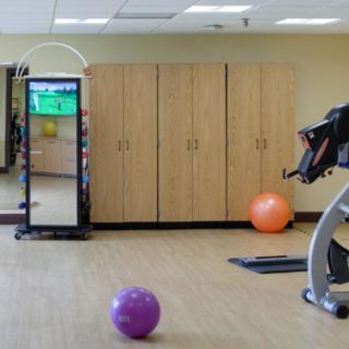 A gym room featuring a stationary bike, fitness balls, large mirror, and storage cabinets.