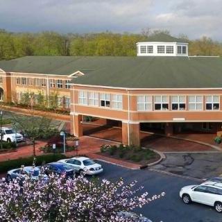 A view of a modern brick building with a surrounding parking lot and cars, set against a backdrop of trees.