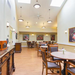 A well-lit dining area with tables and chairs, adorned with paintings and skylights.