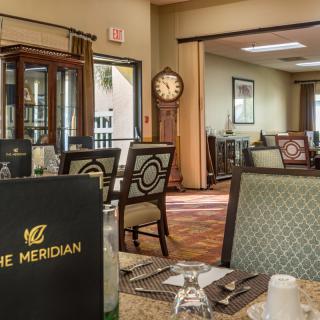 Interior of a dining area with neatly arranged tables and chairs, featuring a menu that reads 'The Meridian' and a large standing clock in the background.
