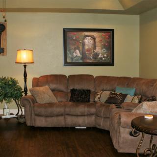 A cozy living room with a sectional couch, floor lamp, and framed painting on the wall.