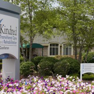 A healthcare facility with a prominent sign and well-maintained landscaping, featuring colorful flowers and trees.