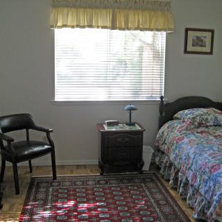 A simple bedroom with a bed, chair, and colorful rug.