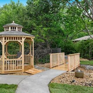 A charming wooden gazebo in a landscaped garden with a small bridge and pathway.