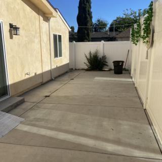 A sunny backyard with a concrete patio and surrounding fence.