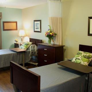 A shared nursing home room with two hospital beds and comfortable furnishings.