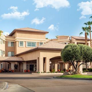 A large residential building with a welcoming entrance, surrounded by palm trees on a sunny day.