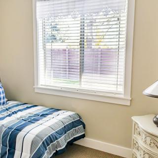 A cozy bedroom featuring a bed with striped bedding, a window with blinds, and a nightstand with a lamp.