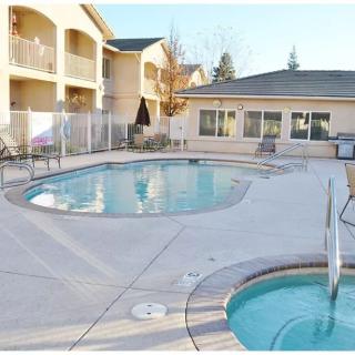 A serene outdoor swimming pool and jacuzzi at an apartment complex on a sunny day.