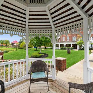 A picturesque view from inside a gazebo overlooking a well-maintained garden with lush green lawns and a brick building in the background.