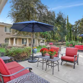A cozy outdoor patio with comfortable seating and a large umbrella, surrounded by greenery.