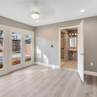 A modern, empty bedroom with wooden flooring and French doors leading to the outside.