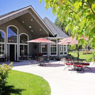 A beautiful house with a spacious outdoor patio, featuring tables, chairs, and umbrellas on a sunny day.