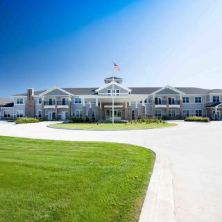 A large, luxurious mansion with a sprawling lawn and circular driveway under a clear blue sky.