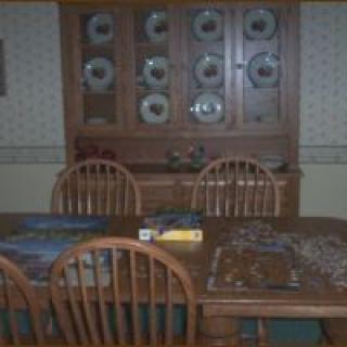 A dining room with a wooden table and chairs, featuring a cabinet and puzzles in progress.