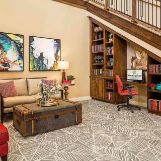 A cozy living room with a computer desk nestled under the stairs, surrounded by decor and artwork.