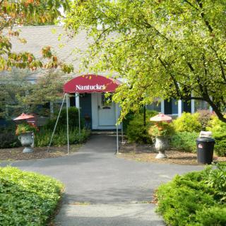 A quaint restaurant entrance with a red awning surrounded by greenery and trees.