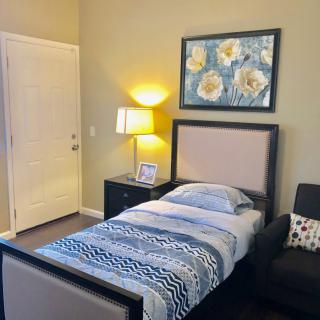 A cozy bedroom with a single bed, bedside table, lamp, and floral artwork on the wall.