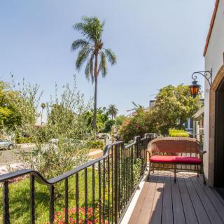 A sunny balcony with a view of a garden and palm tree.