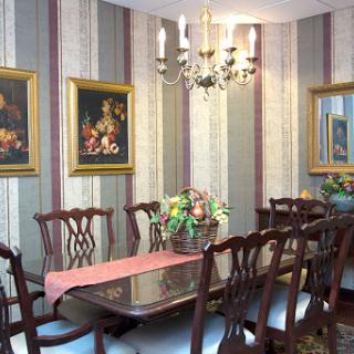 An elegant dining room featuring a long table, classic wooden chairs, and decorative wall art.
