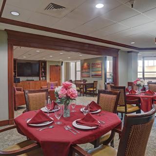 A well-appointed dining room with elegantly set tables featuring red tablecloths and floral centerpieces.