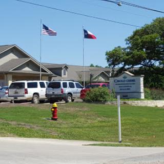 A facility in Texas with American and state flags flying, surrounded by vehicles and green grass.