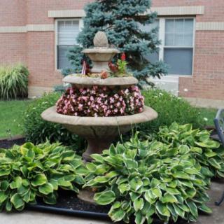 A decorative garden fountain surrounded by vibrant flowers and lush hosta plants.