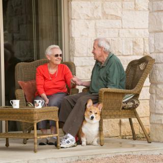 An elderly couple enjoying a conversation on the patio with their dog.