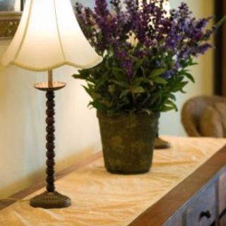 A decorative table setup featuring a table lamp and a potted plant with purple flowers.