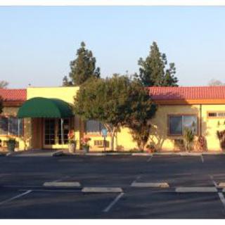 A yellow building with a green awning, surrounded by trees, and an empty parking lot.