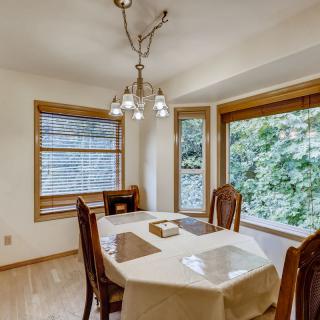 A cozy dining room with a chandelier, surrounded by large windows and featuring a table set for four.