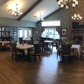A cozy dining room with elegant chandeliers and a fireplace, featuring multiple tables and chairs on a wooden floor.