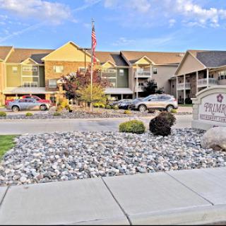 A view of a well-maintained apartment complex with landscaping and parked vehicles under a clear sky.