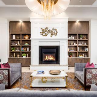 A modern living room features a central fireplace, flanked by built-in shelves, comfortable sofas, and a stylish coffee table under a striking chandelier.