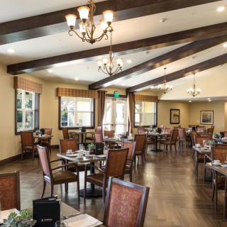 A spacious and elegant restaurant interior featuring wooden tables and chairs, with chandeliers providing ambient lighting.