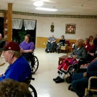 A group of elderly people in a nursing home, many seated in wheelchairs.