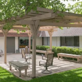 A tranquil patio area with a pergola, surrounded by greenery and furnished with outdoor seating.