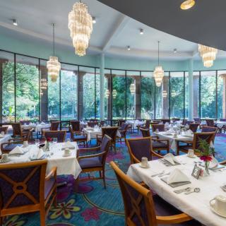 An elegant dining room with beautifully set tables and large windows overlooking the greenery.