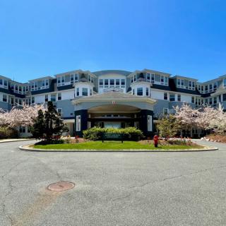 A large, multi-story hotel with a grand entrance surrounded by blooming trees against a clear blue sky.