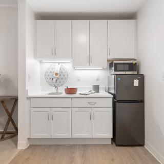 A compact modern kitchen with white cabinetry, a microwave, and a small refrigerator.