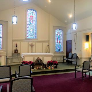 A peaceful chapel interior featuring an altar with decorations, surrounded by seating and illuminated by stained glass windows.